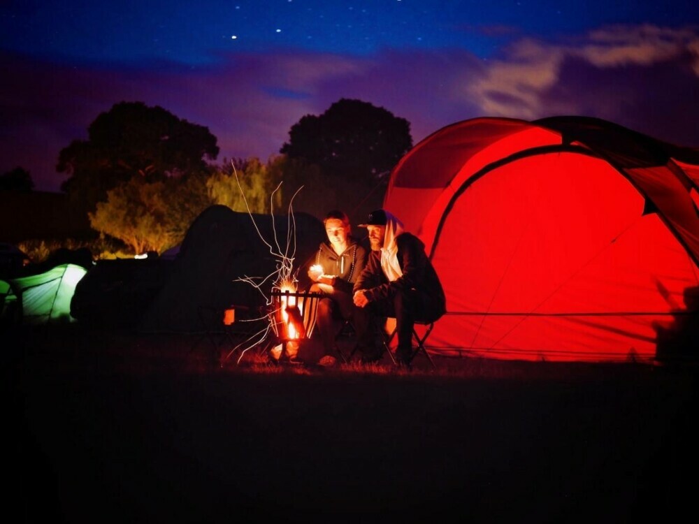 Campers by a campfire and tent at night